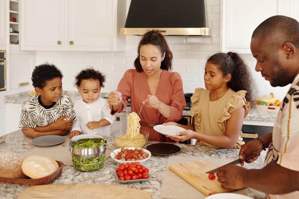 Family enjoying a cooking session together in a modern kitchen, preparing pasta and vegetables.